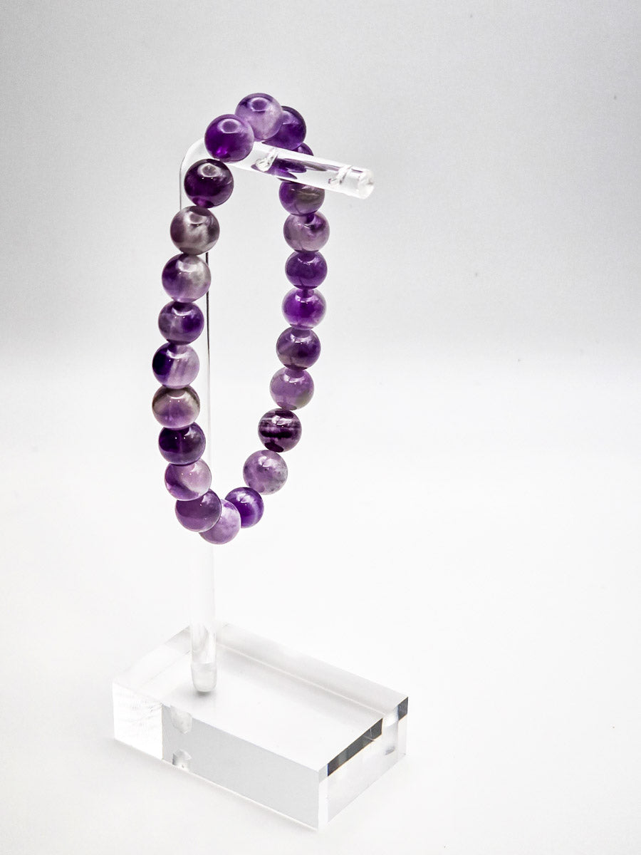 Amethyst bracelet perched on a clear acrylic stand, emphasizing the bracelet's elegance and the stone's 'master healer' qualities.