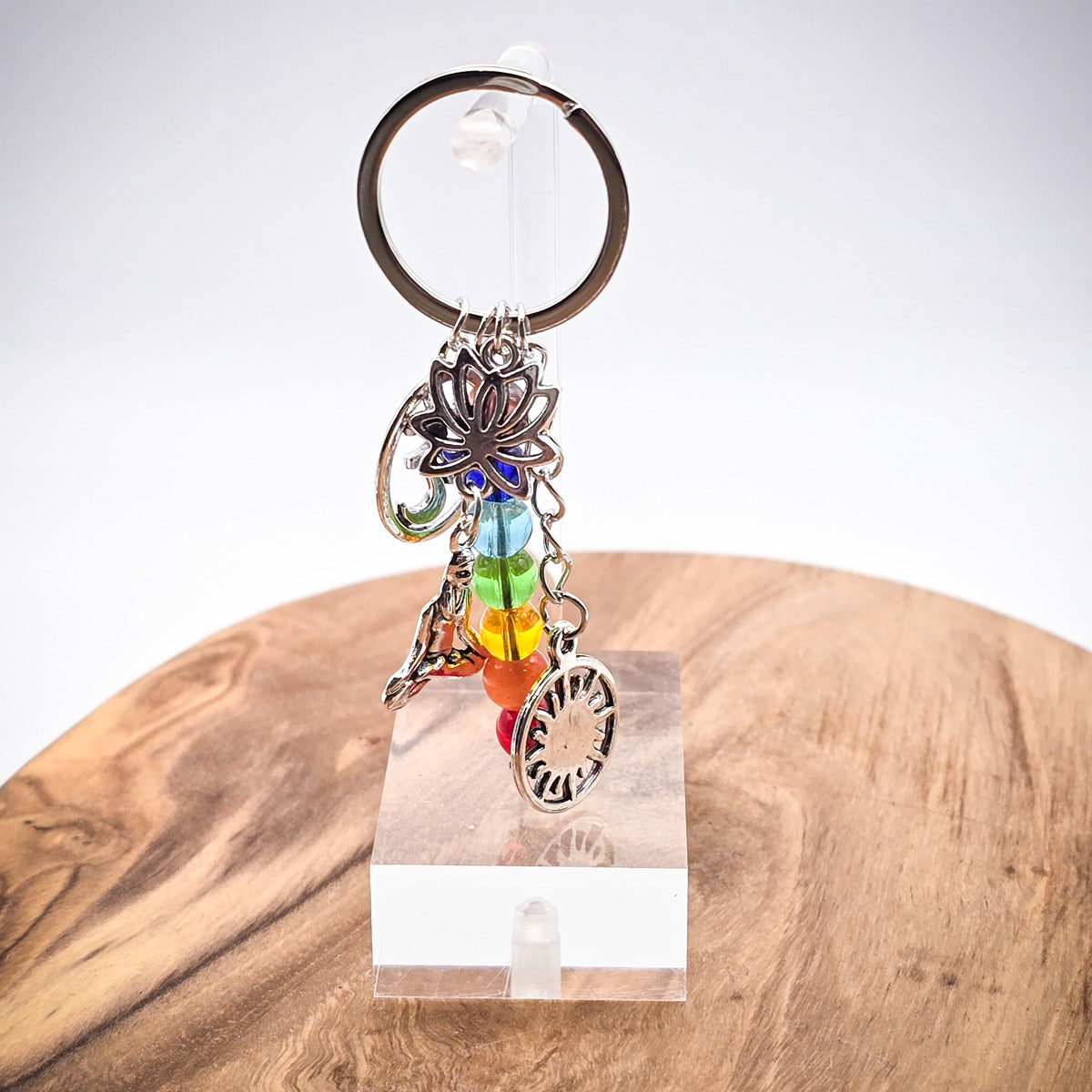 Chakra Keychain with rainbow beads and yoga-inspired charms including an Ohm symbol, meditating woman, lotus flower, and sun, on a clear acrylic stand, on a wood board