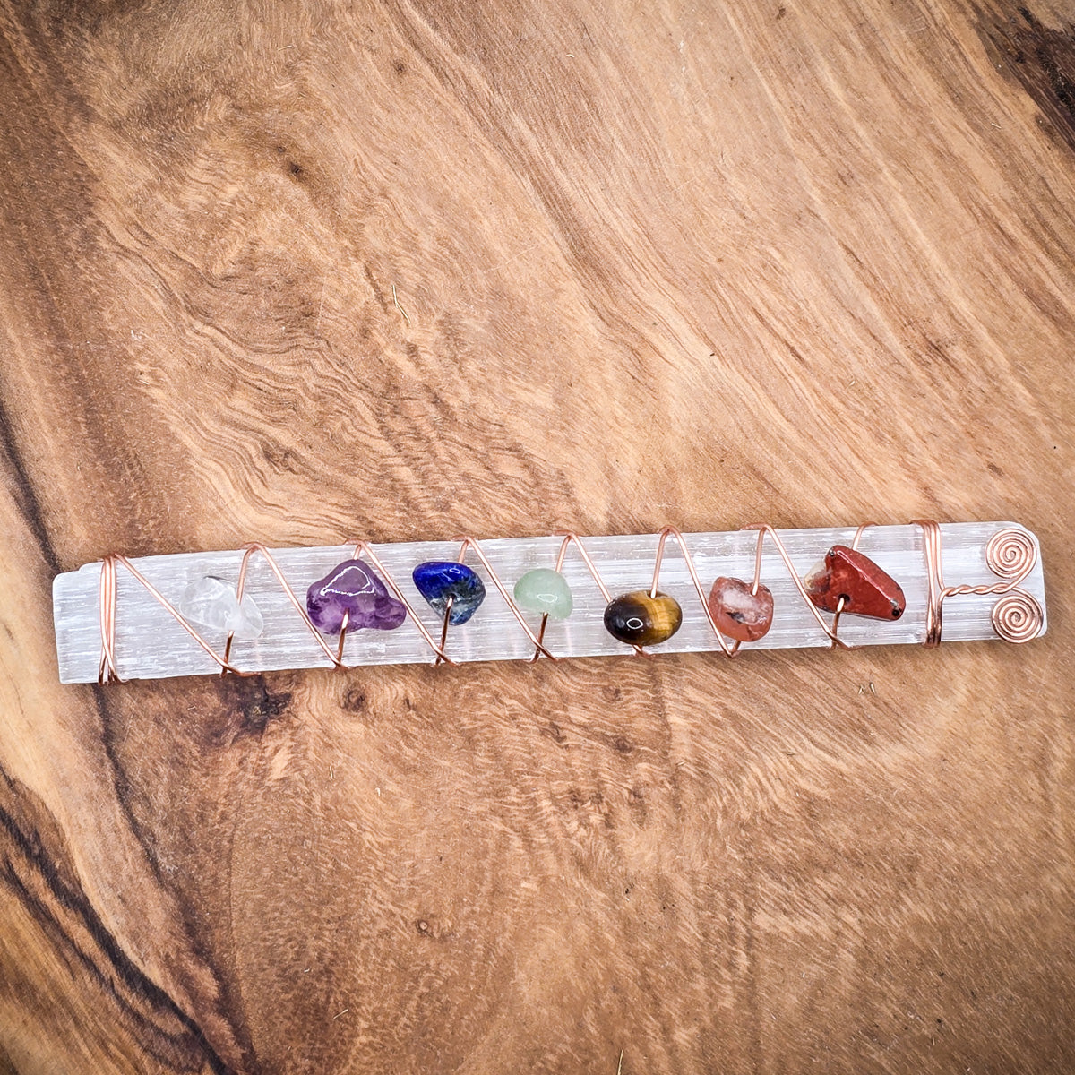 Chakra Healing Selenite Wand with crystal chips for meditation and serene energy.  laying on a wood panel, slightly zoomed out view