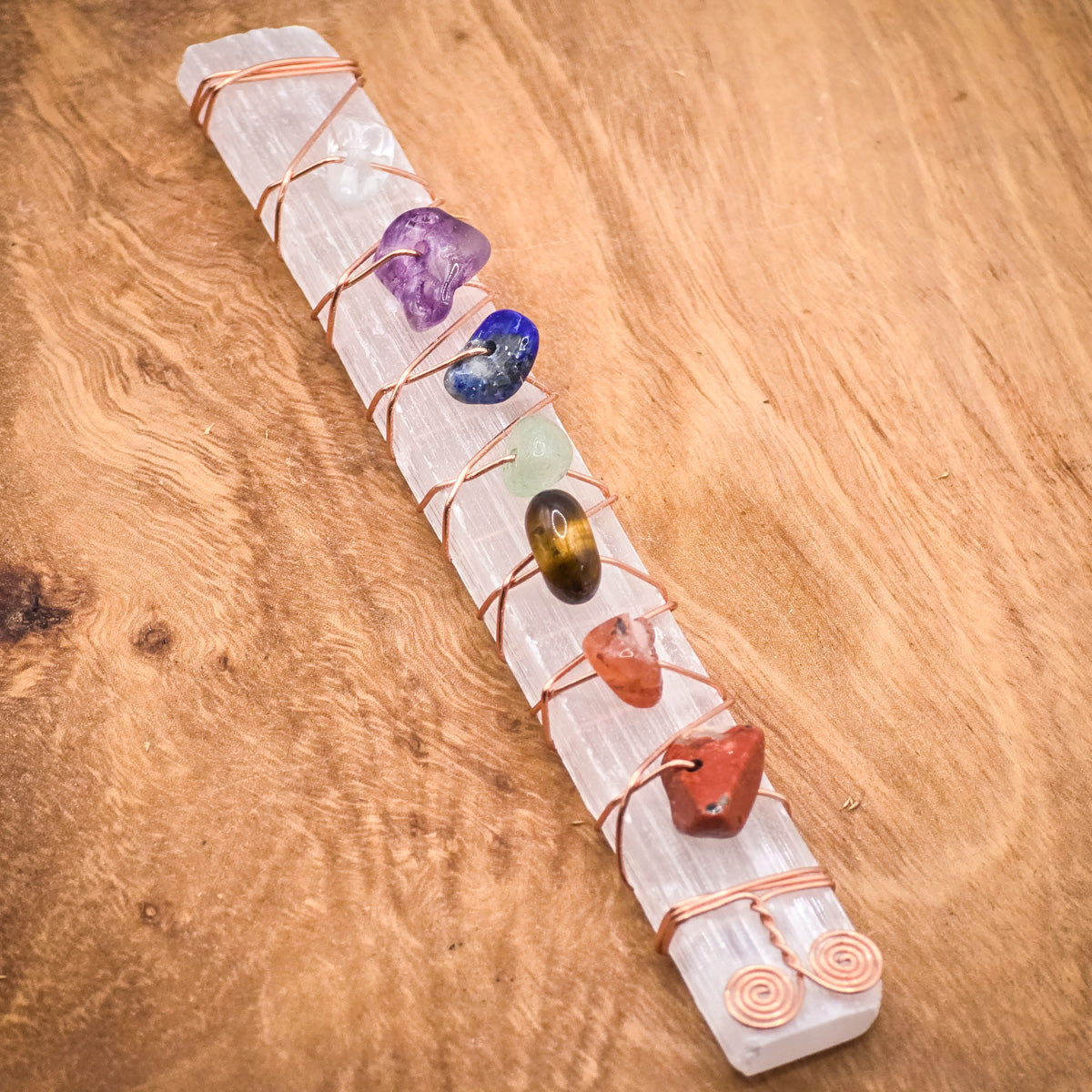 Chakra Healing Selenite Wand with crystal chips for meditation and serene energy, closeup laying on a wood panel