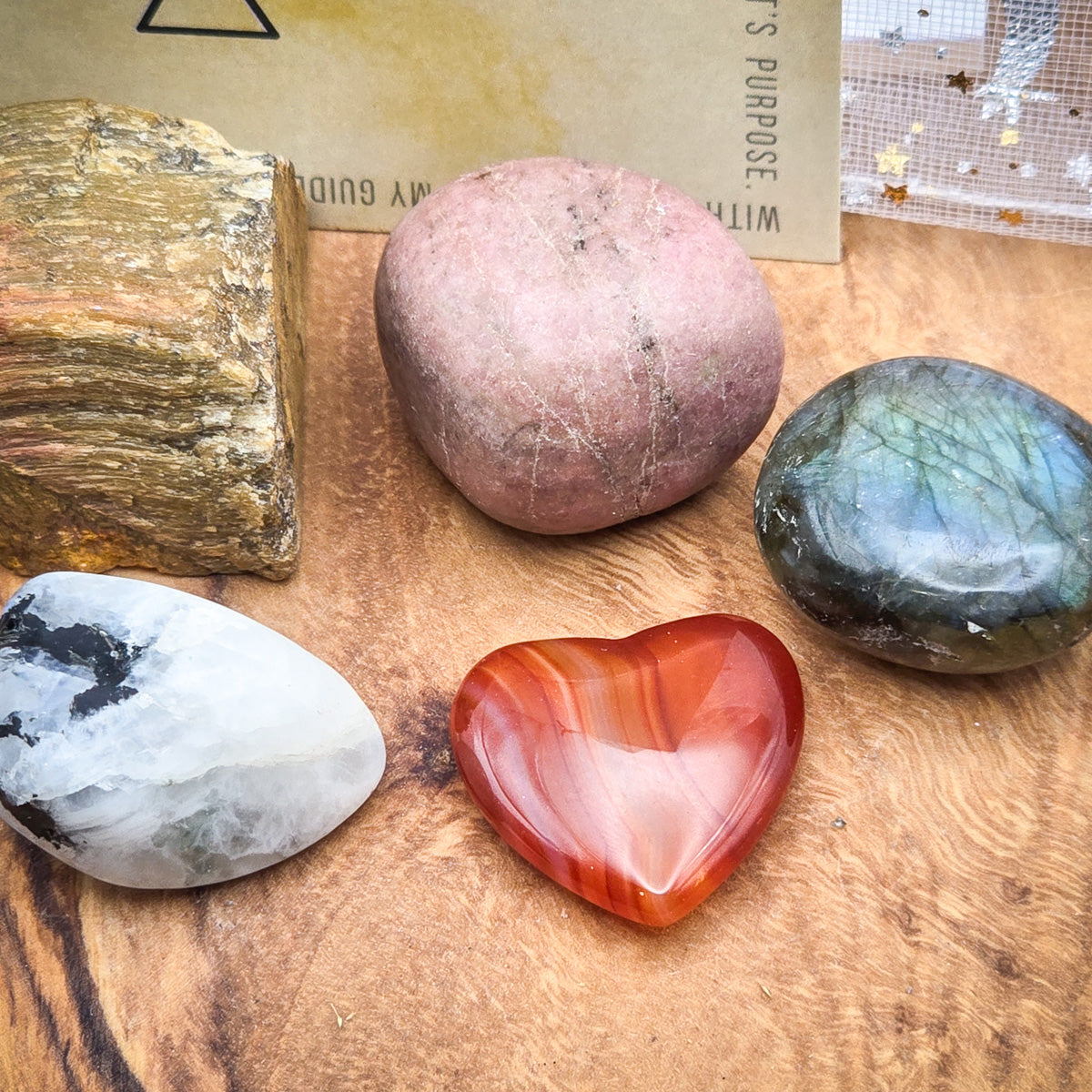 Assortment of Labradorite, Rhodonite, Tiger's Eye, and Moonstone for Leo, close up of all stones on a wood panel