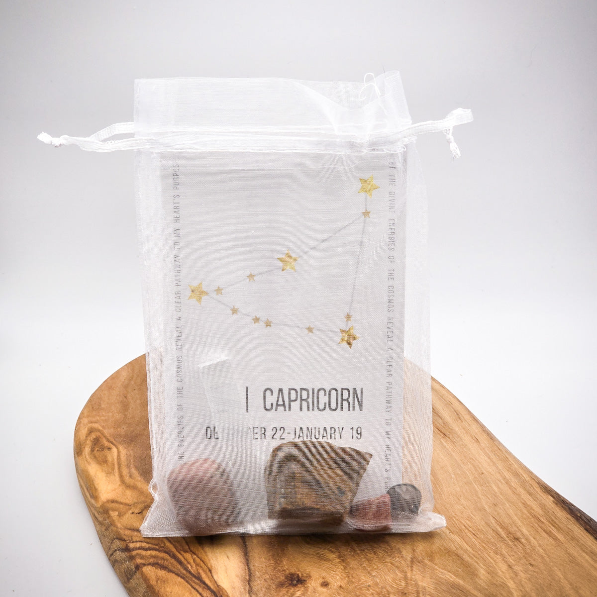 Capricorn Zodiac Stone Bag with Birthstone and Guide Card, all contents inside a bag, on a wood panel, white background.