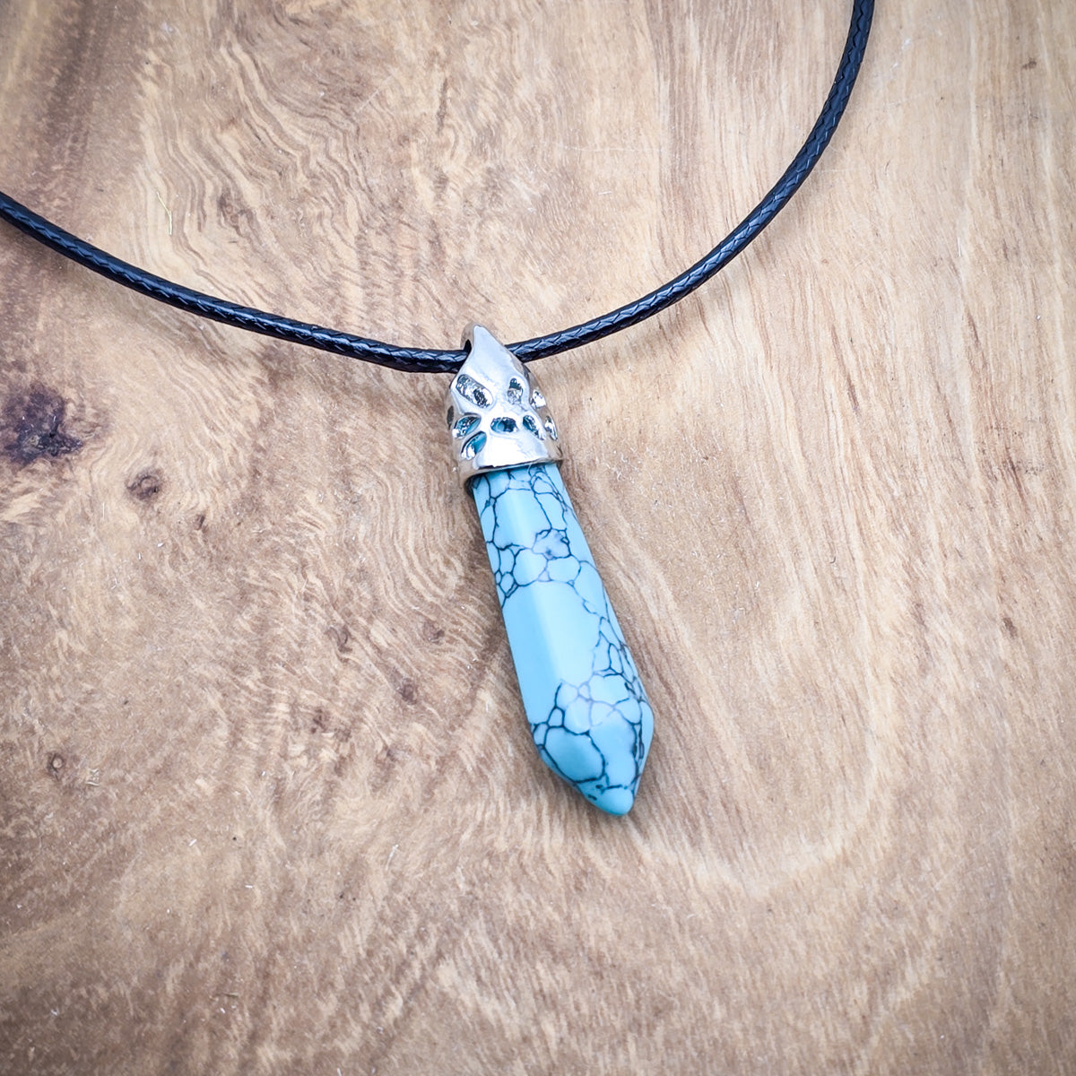 Turquoise hexagonal column pendant on black cord, displayed on wood, showcasing its bright color and polished surface.