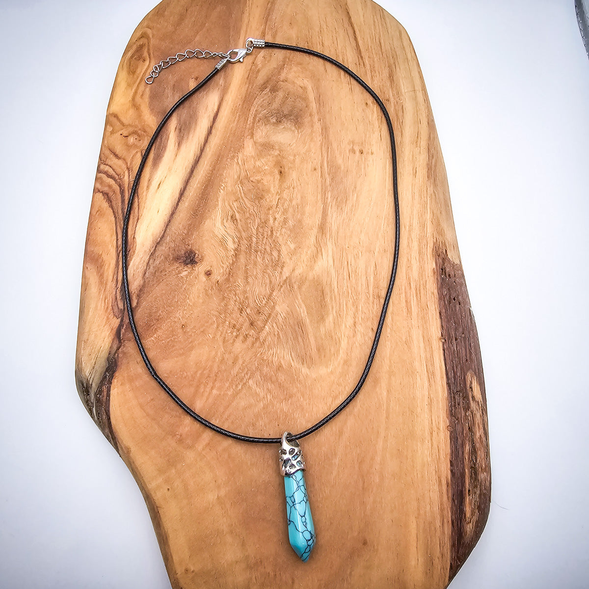 Full view of the Turquoise pendant necklace against a wood plank, emphasizing the elegance of the black cord and the pendant's captivating color.