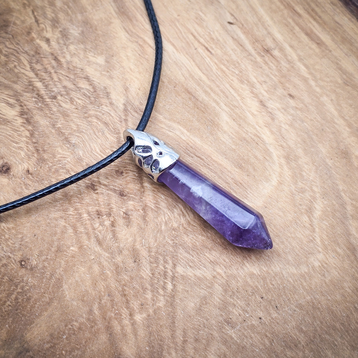 Amethyst hexagonal column pendant on black cord, showcased on a wooden background to highlight its rich violet color and polished finish.