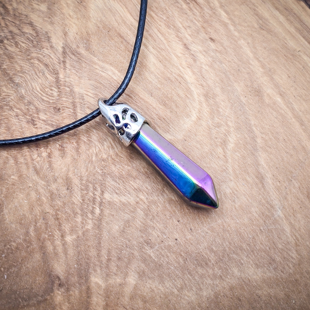 Titanium Aura Quartz hexagonal column pendant on black cord, displayed on wood, showcasing its radiant colors and polished finish.