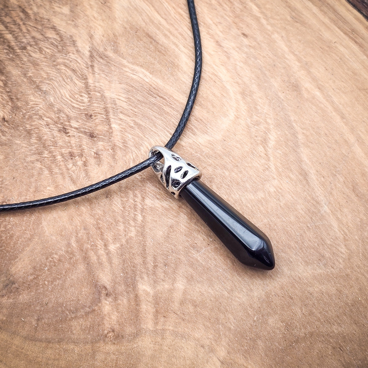 Onyx hexagonal column pendant on black cord, presented on wood, showcasing its deep black elegance and polished geometry