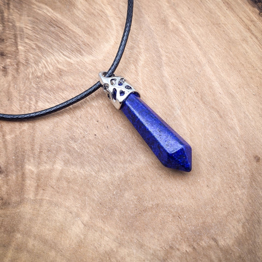 Lapis Lazuli hexagonal column pendant on black cord, against a wooden backdrop, showcasing its deep blue hues and natural golden pyrite inclusions.