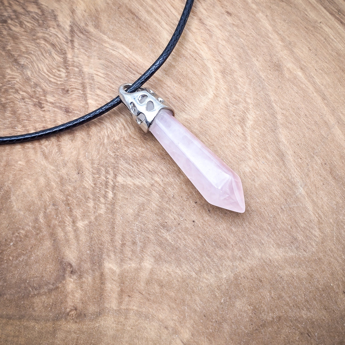 Rose Quartz hexagonal column pendant on black cord, against a wooden background, accentuating its soft pink hue and polished finish.