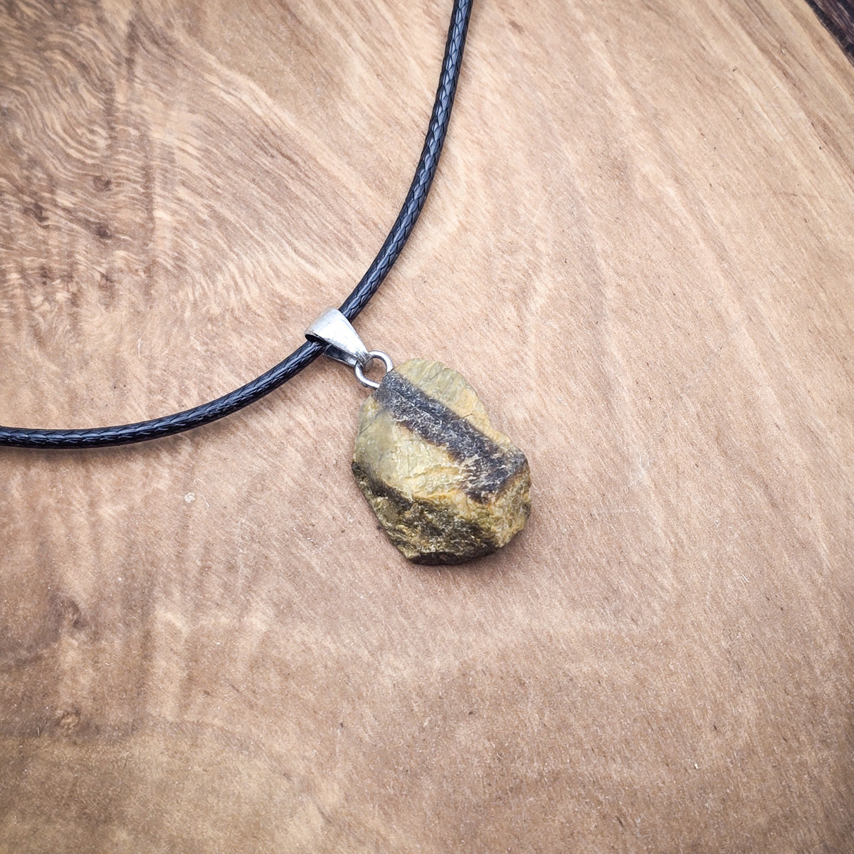 Tiger's Eye raw gemstone pendant on black cord, against a wooden backdrop, showcasing its mesmerizing bands and silky sheen.