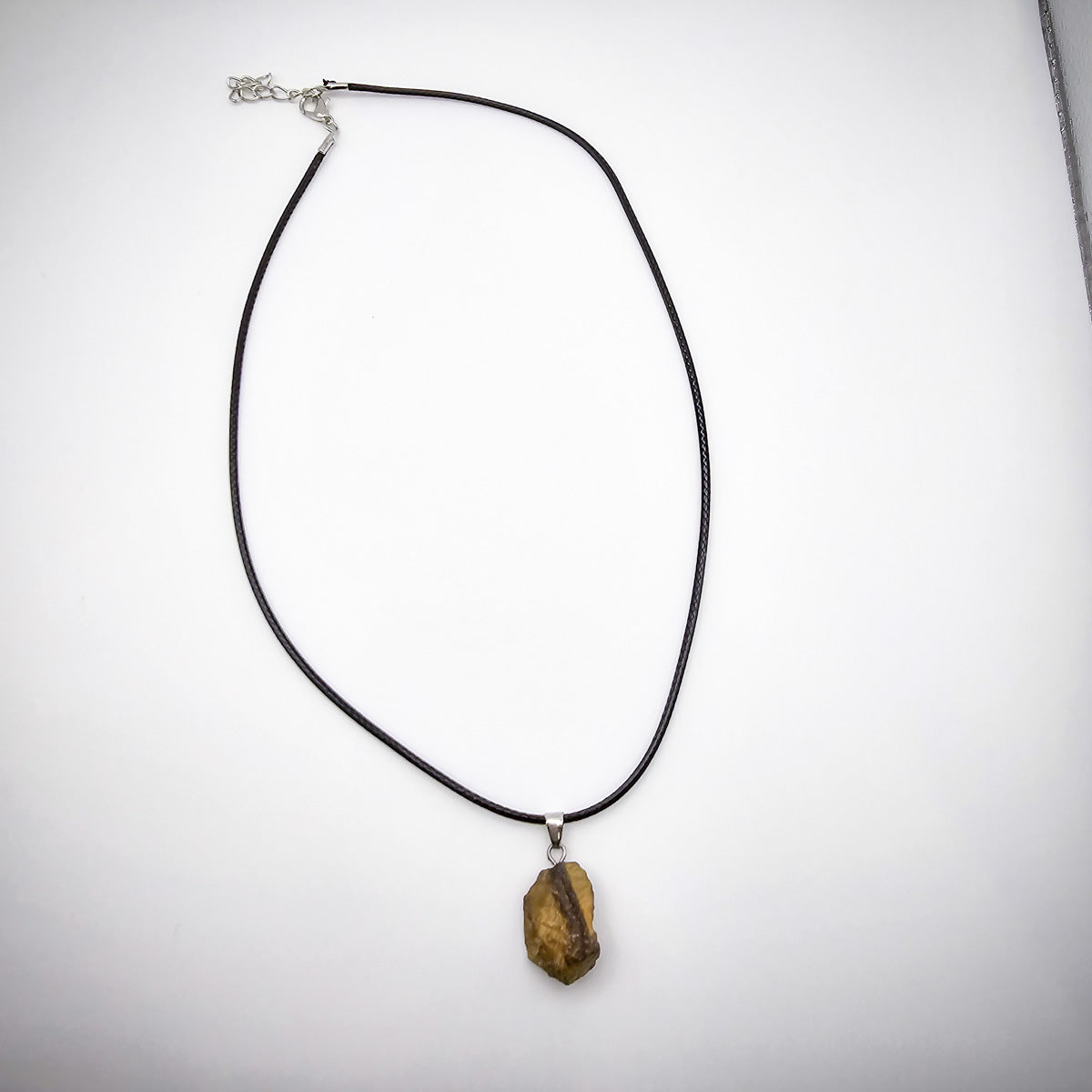 The entire Tiger's Eye pendant necklace displayed against a white background, illustrating the elegance of the black cord and the vibrant, protective stone.