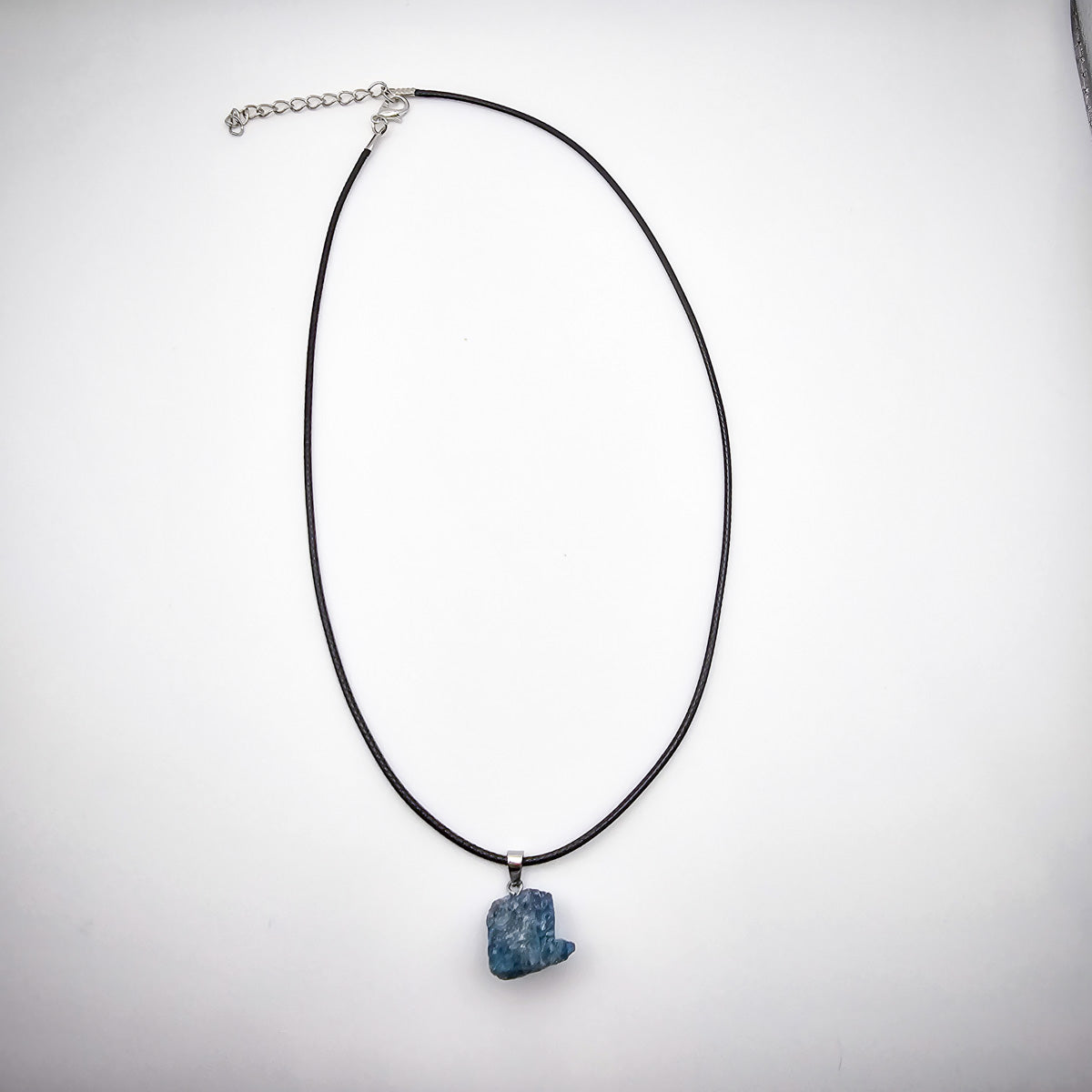 Entire view of the Blue Apatite pendant necklace on a white background, displaying the black cord and the captivating blue gemstone.