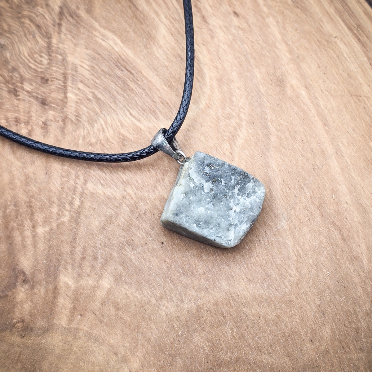 Lapis Lazuli raw gemstone pendant on black cord against a wood background, showcasing natural beauty."