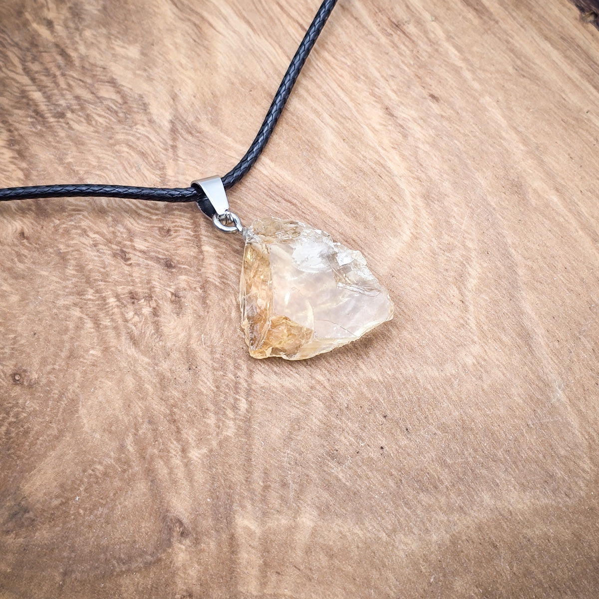 Citrine raw gemstone pendant on black cord, showcased on wood for a natural, radiant display of its sunny hues.