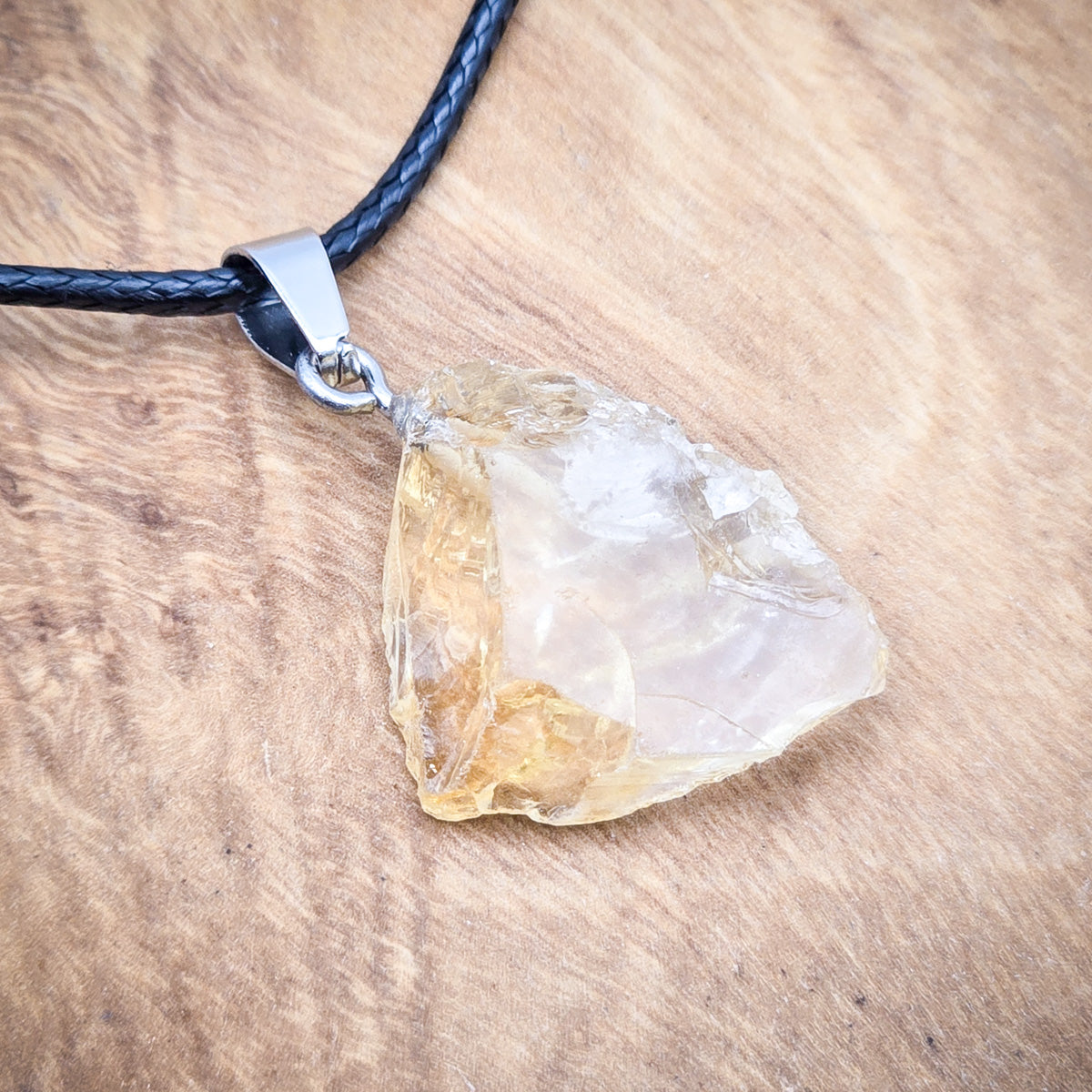 Close-up view of the Citrine pendant, highlighting its unique texture and vibrant golden colors.Entire Citrine pendant necklace against a white background, accentuating the black cord and the gem's natural brilliance.