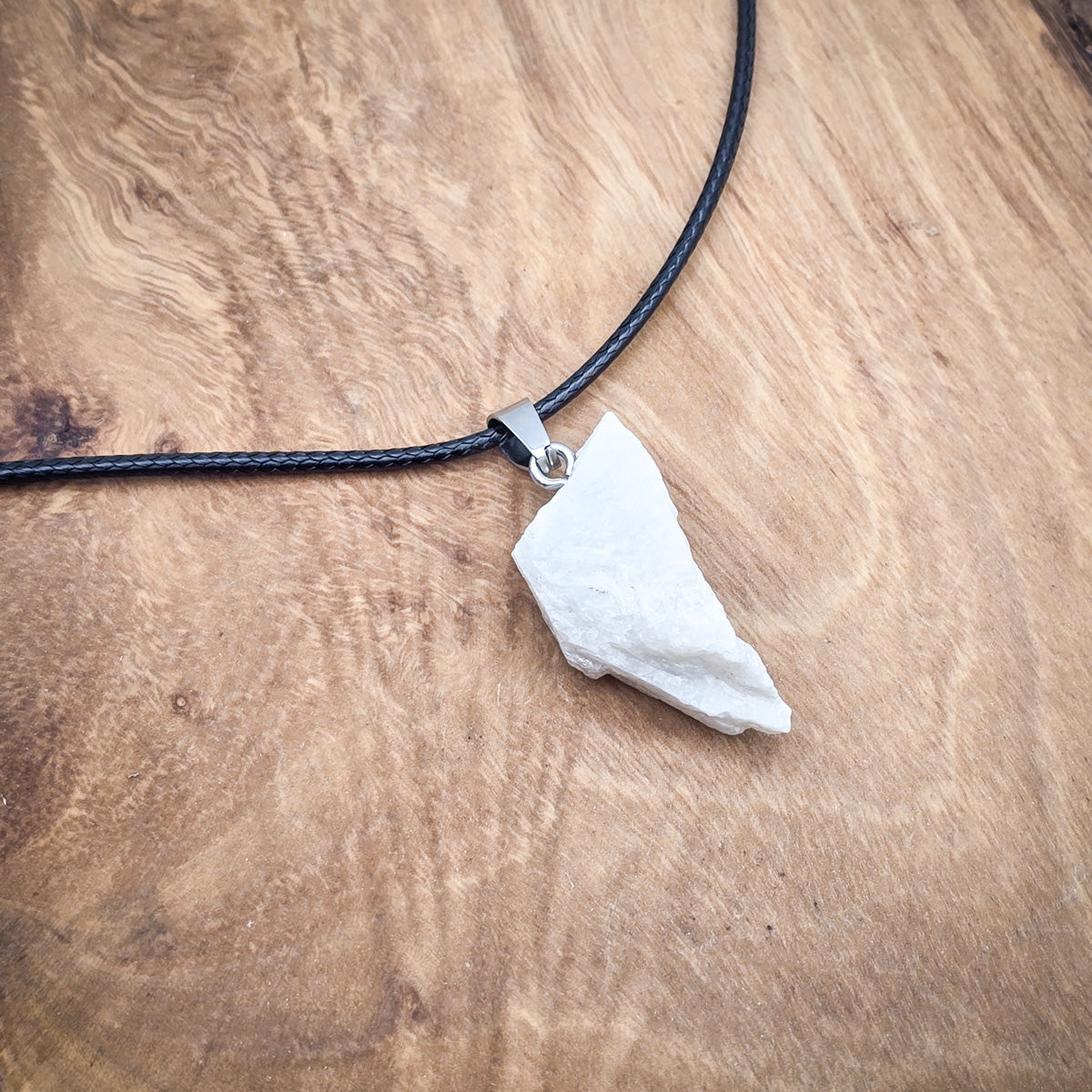 Moonstone raw gemstone pendant on black cord over wood, highlighting its natural luminosity and unique variations.