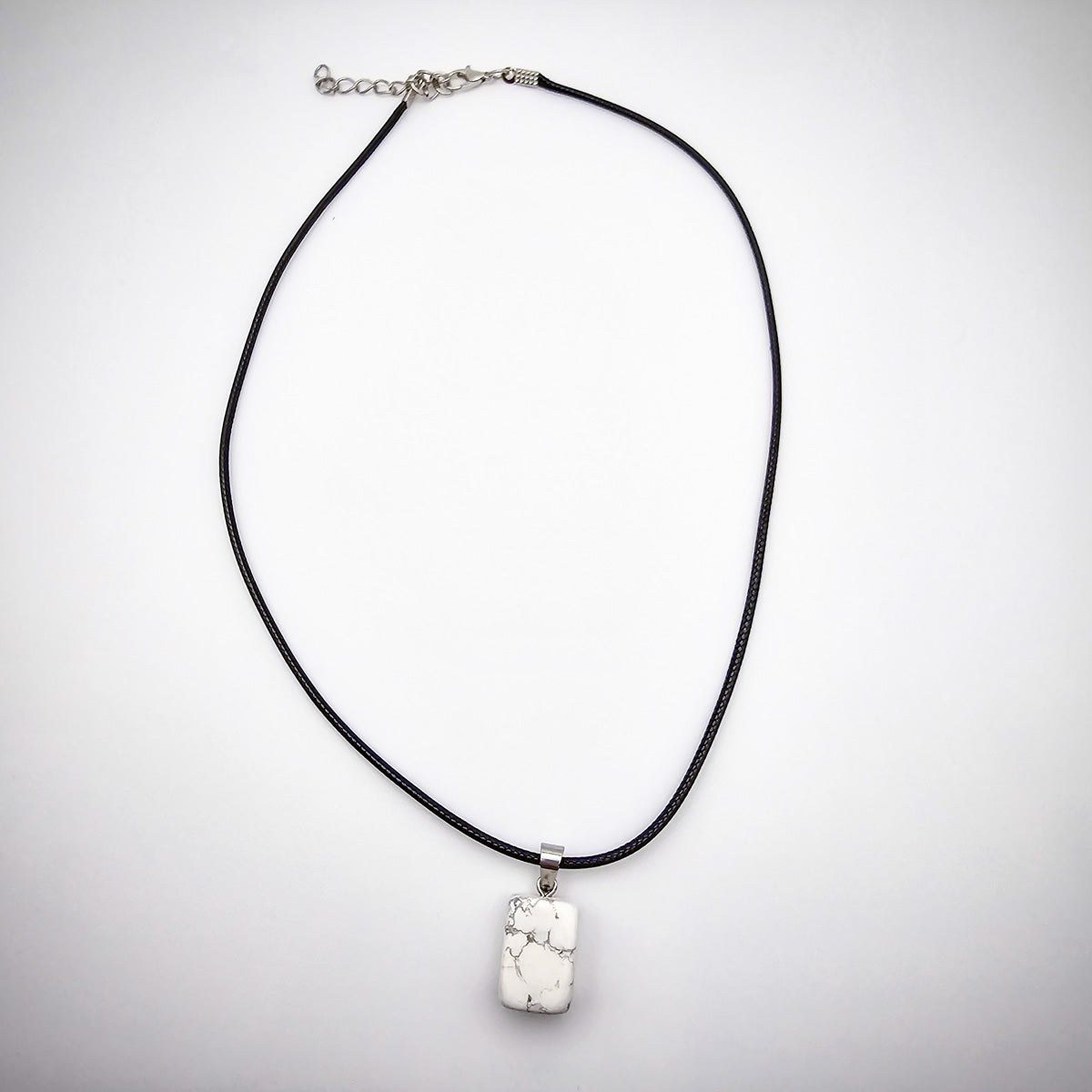 Full view of the Howlite cube gemstone pendant necklace against a white background, emphasizing the sleek black cord and minimalist elegance.