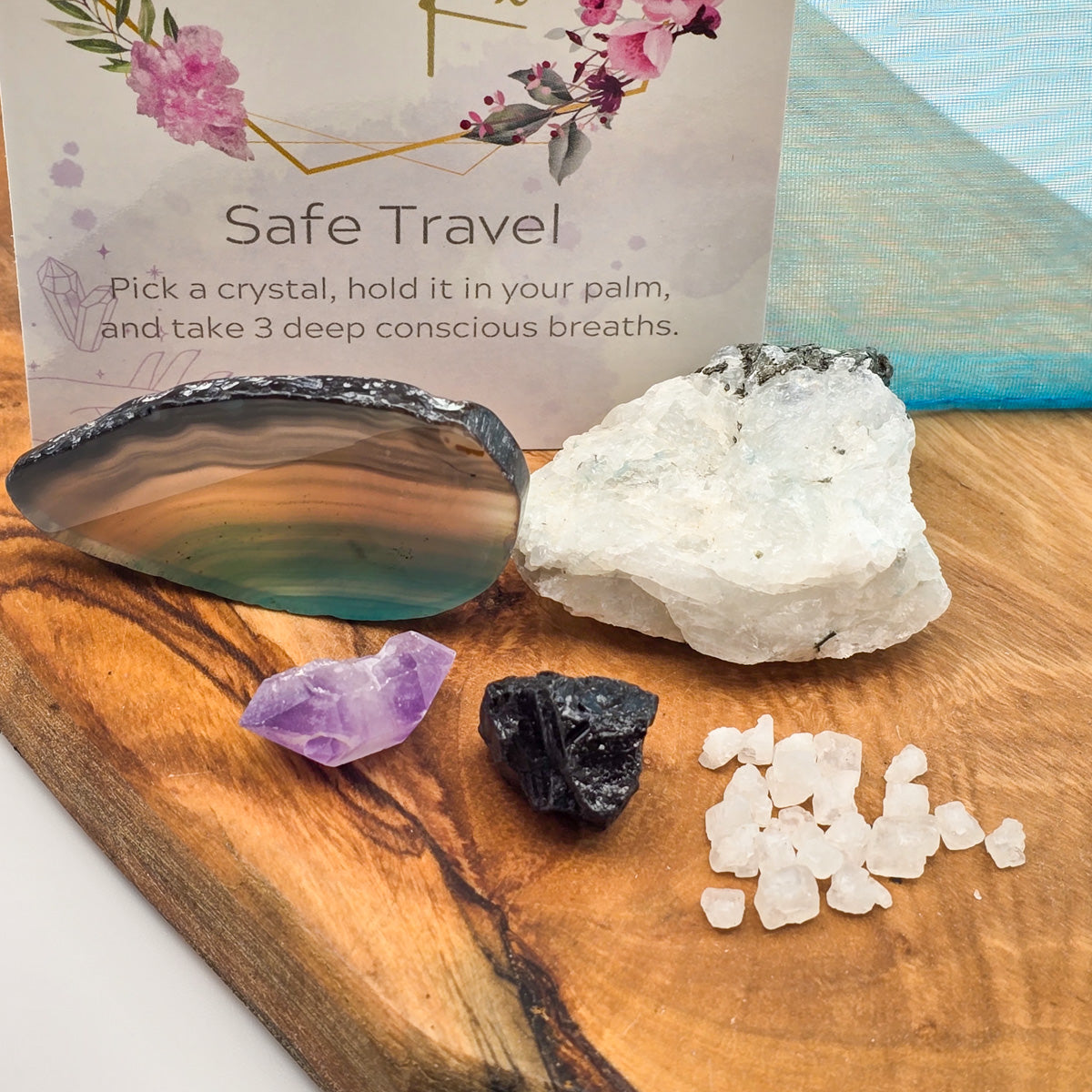 Close-up shot of 'Safe Travel' Mojo Bag's crystals on a wood panel, with the bottom of the card featuring the title 'Safe Travel' visible on the left side